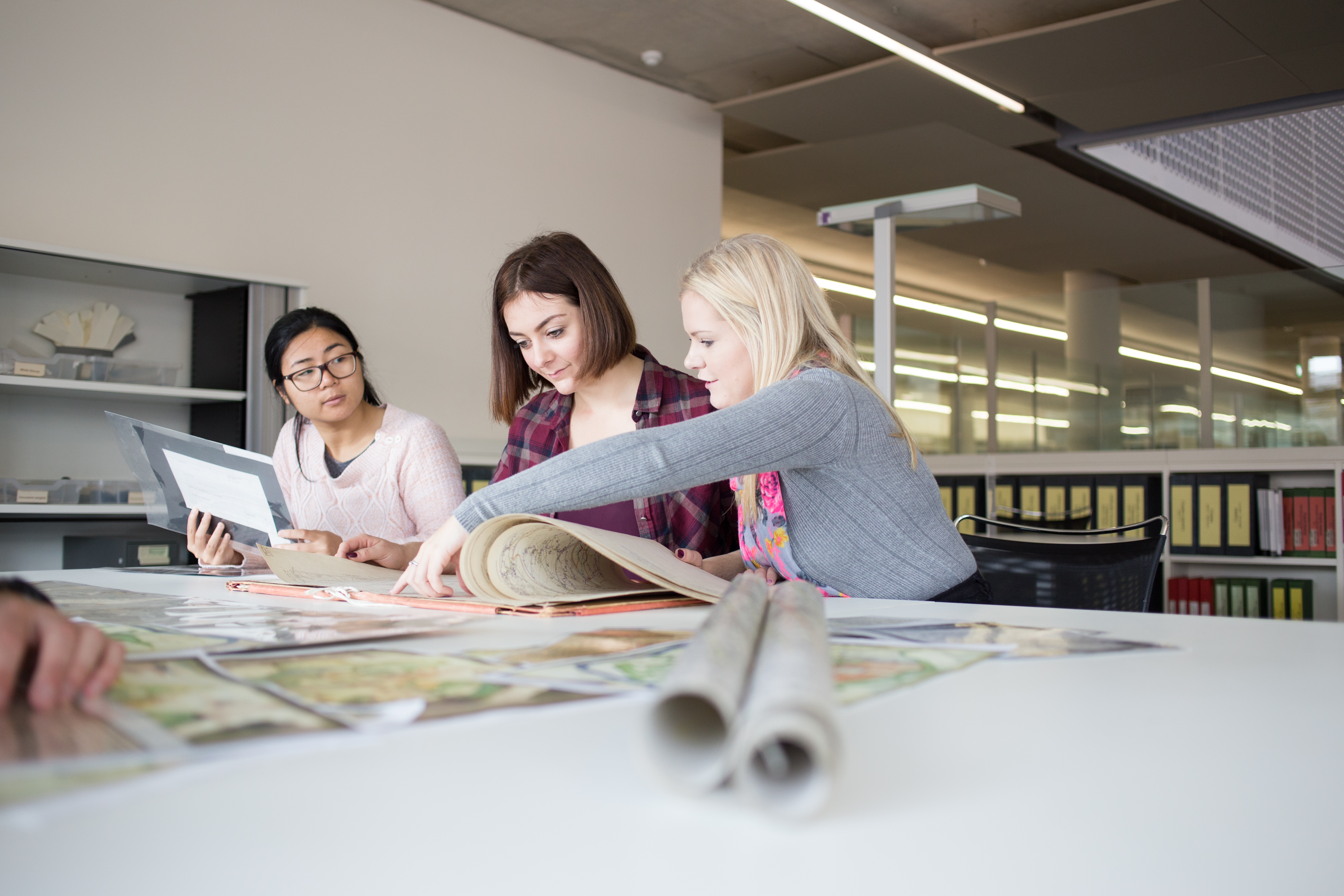 Image of three students working at a table in the library, papers spread out in front of them.